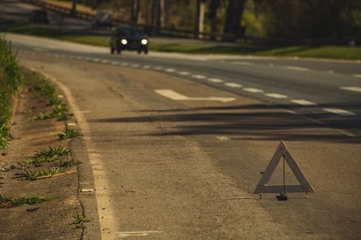 voiture arrêtée sur la bande d'arrêt d'urgence d'une autoroute, feux de détresse allumés, triangle de signalisation posé à l'arrière, conducteur en gilet jaune à côté du véhicule