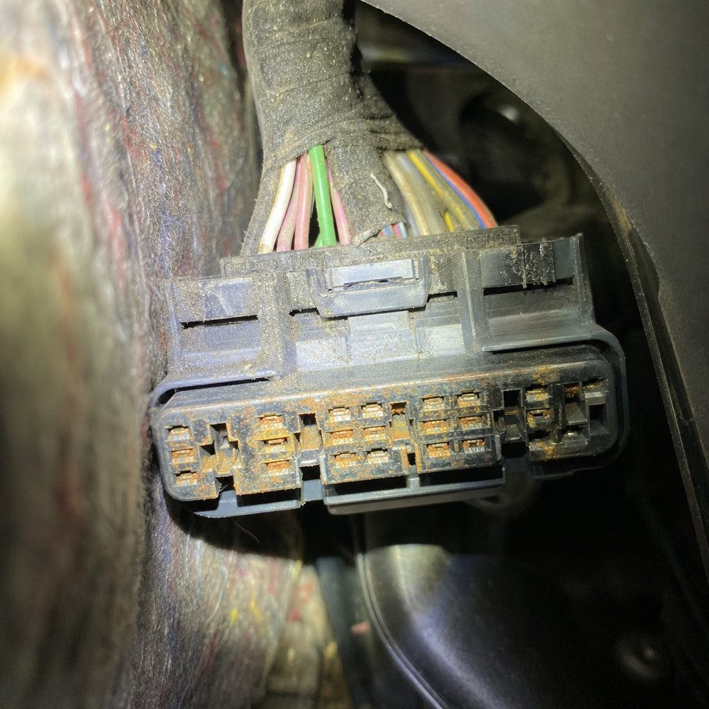 gros plan sur un connecteur de faisceau électrique oxydé sous le tableau de bord d'une petite citadine, lampe frontale éclairant la zone