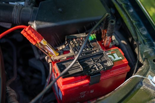 multimètre numérique affichant une valeur de tension sur les bornes rouge et noire d'une batterie de voiture, capot moteur ouvert, éclairage d'atelier
