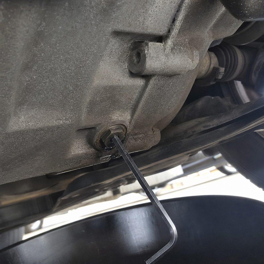 bouchon de vidange hexagonal sous le carter d'une boîte manuelle Mini Cooper, clé Allen insérée, bac de récupération d'huile positionné en dessous