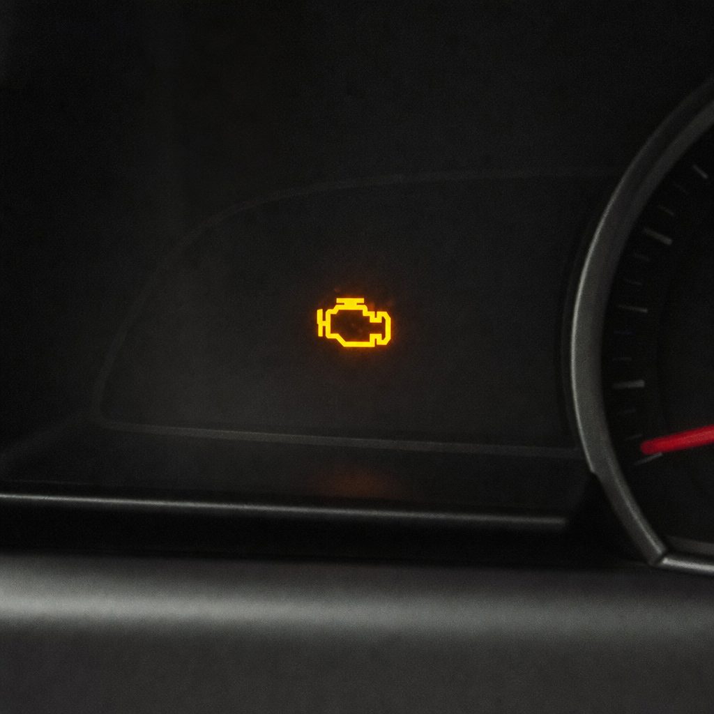 tableau de bord de voiture avec le voyant moteur orange allumé, éclairage intérieur sombre, focus net sur le symbole moteur